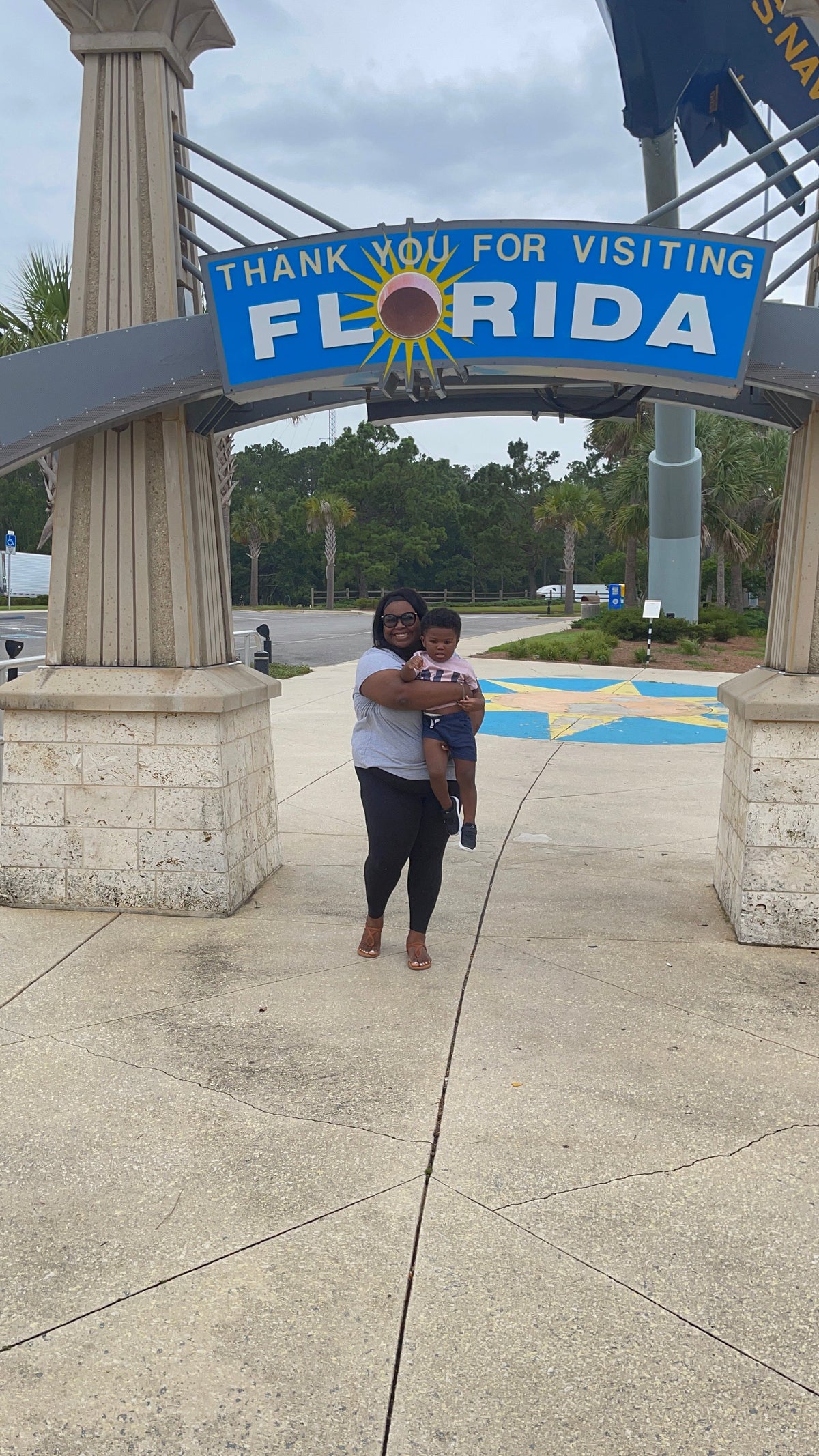 An adult holding a young child beneath a “Thank you for visiting Florida” sign during the family’s 2021 trip.